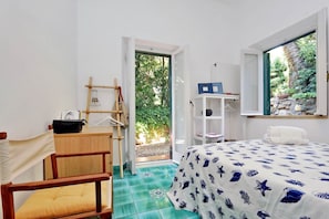 Une chambre à coucher comprenant un lit, un bureau, une chaise, une armoire et donnant sur un espace verdoyant.