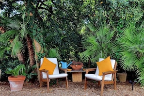 A garden setting with two white chairs, a wooden table, and a potted plant.