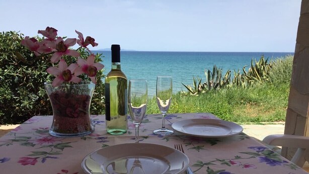 Une table dressée pour deux personnes, avec une nappe à motifs floraux, une bouteille de vin, deux verres à vin et un vase rempli de fleurs.