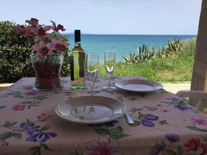 A table set for two with a floral tablecloth, a bottle of wine, two wine glasses, and a vase of flowers. - A quiet house with 800 square metres garden on the sea (Sorso)