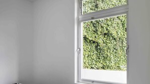 Ein Schlafzimmer mit einem Einzelbett, einem Fenster mit Blick ins Grüne und weißen Wänden.