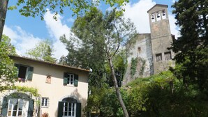 Un edificio rústico con un campanario, rodeado de follaje y un carro de madera.