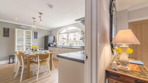 A modern kitchen with a dining area, featuring a large window, wooden cabinets, and a dining table set for four. - Kipling House (8), Wells-next-the-Sea, Norfolk (Wells-next-the-Sea)