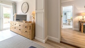 A modern living room with a wooden TV stand, a clock, and a dining area visible through an open door. - Kipling House (8), Wells-next-the-Sea, Norfolk (Wells-next-the-Sea)
