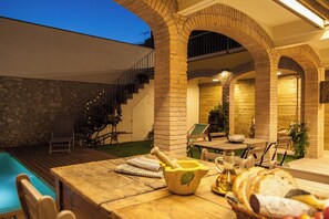 A poolside area with a wooden table, a stone wall, and a staircase leading to an upper level. - Farmhouse in a nice wine region 40 mins to Barcelona and 25 to Sitges beaches. (Subirats)
