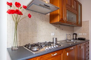 A kitchen with a gas stove, wooden cabinets, a stainless steel sink, and a tiled backsplash.