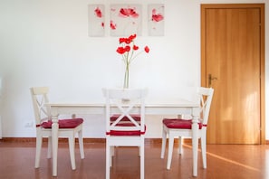 Ein Essbereich mit einem weißen Tisch und Stühlen, einer Vase mit roten Blumen und einer Holztür.