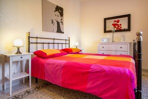 A bedroom with a bed, bedside tables, a nightstand, a dresser, a lamp, a framed picture, and a vase with flowers.