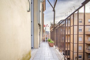Un étroit couloir résidentiel, doté d’un sol carrelé, d’une rambarde métallique d’un côté et d’une rangée de plantes en pot.