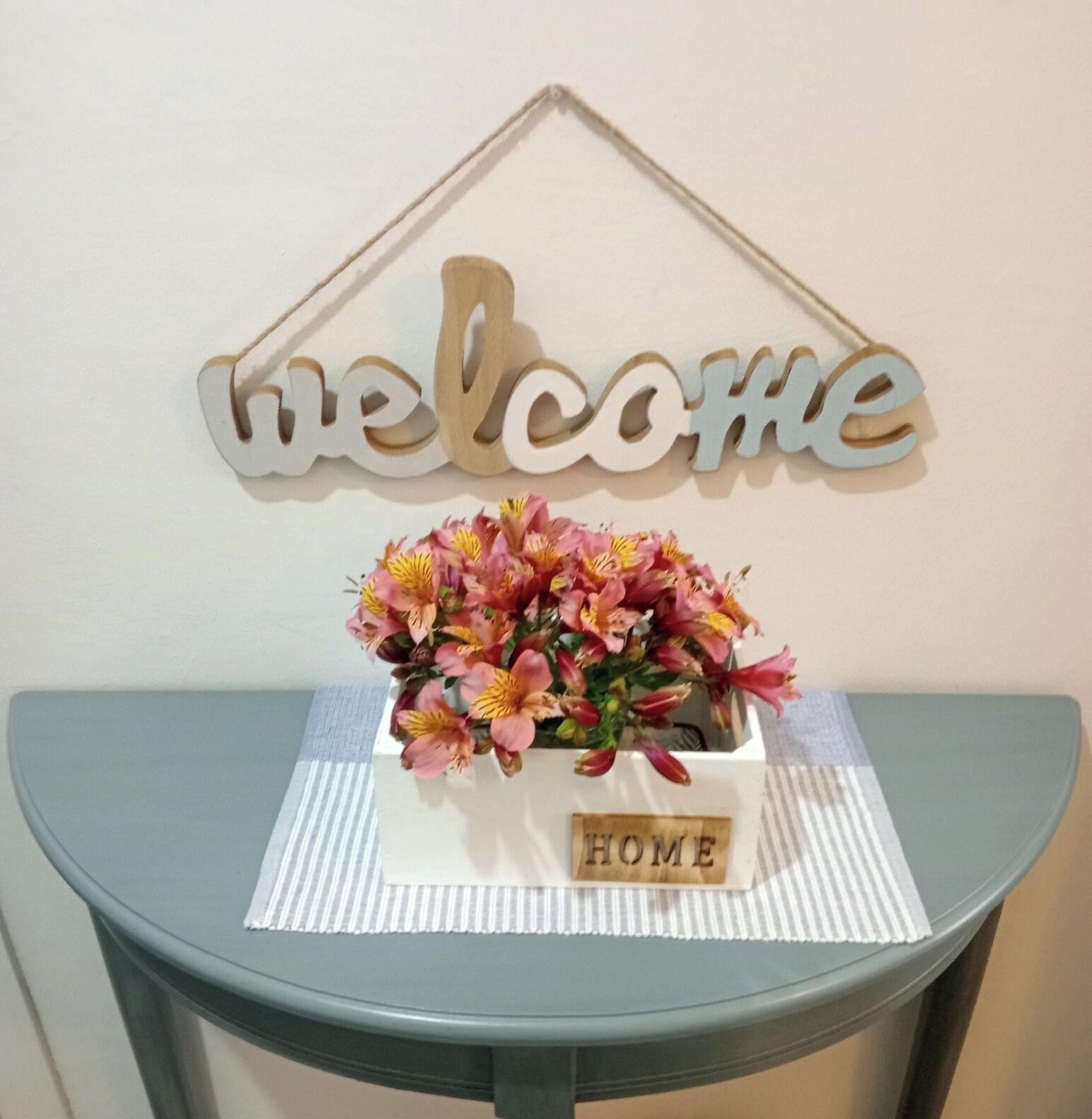 A welcome sign, a floral arrangement, and a placard with 'HOME' on a table.