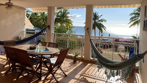 Un balcon avec une table, des chaises, un hamac et une vue sur la plage et l’océan.