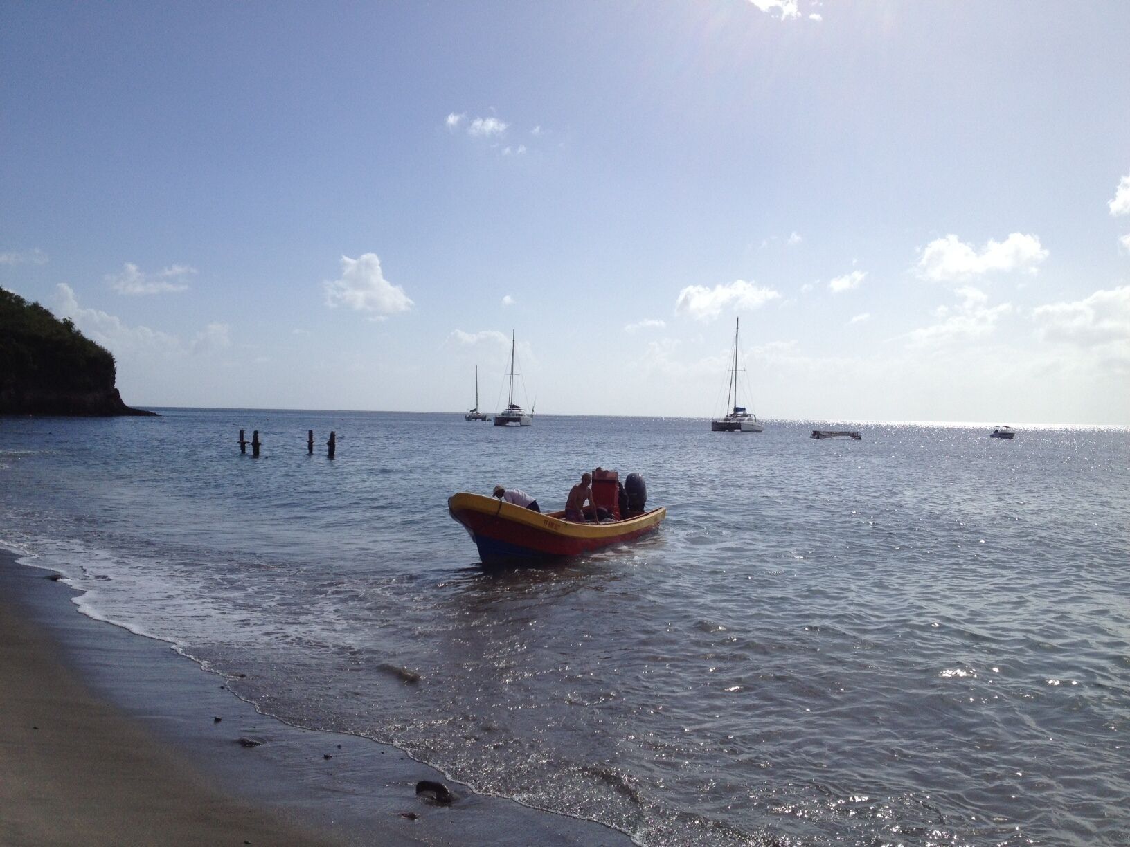 Een strand met rustig water, een klein bootje in de voorgrond en meerdere zeilboten in de verte.