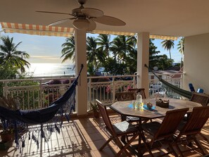 Ein Balkon mit Blick auf den Strand, einer Hängematte, einem Tisch mit Stühlen und einem Deckenventilator.