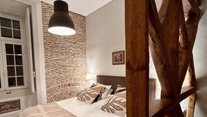 A bedroom with a bed, a hanging light fixture, a wooden beam structure, and a brick wall.