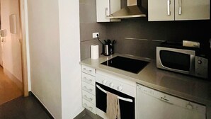 A modern kitchen with white cabinets, a black sink, a stainless steel microwave, and a wooden ceiling.