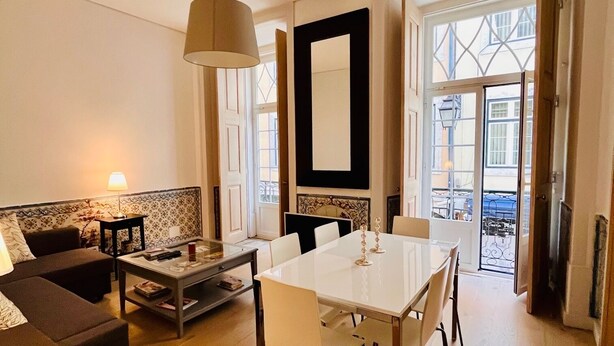 A spacious living room with a dining table, sofa, and a large window offering a view of the city.
