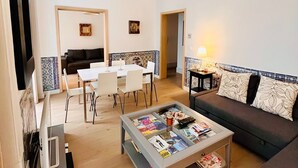 A modern living room with a dining area, a sofa, a coffee table with magazines, and a hanging light fixture.