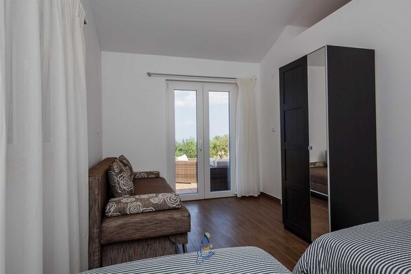 A room with a sofa, a bed, a wardrobe, and a sliding glass door leading to an outdoor area.