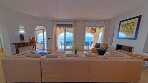 A spacious living room with a large beige sofa, a small wooden table, and a view of the sea through large glass doors. - Villa Rosh, A luxury, 3 floor villa with majestic sea views this large villa is perfect for a large ... (Xàbia)