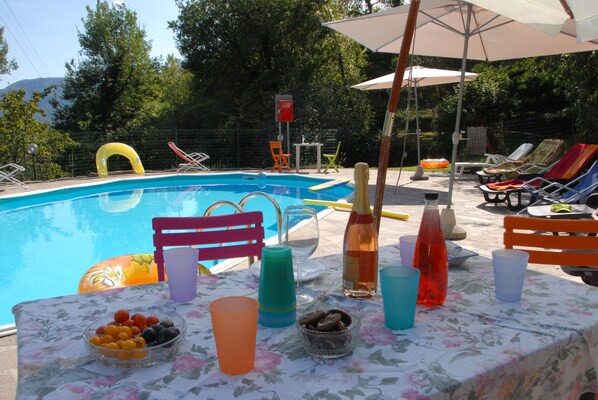 A poolside area with a table set for a meal, surrounded by lounge chairs and umbrellas. - Villa in the green with private pool, garden, wi-fi for families and groups (gallicano)