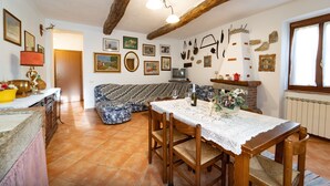 Ein gemütliches Wohnzimmer mit einem Holzesstisch, einer Couch und einem Fernseher. An den Wänden befinden sich Bilder in Rahmen und auf dem Tisch steht eine Lampe.