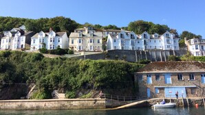 A coastal town with terraced houses, a stone building with a blue door, and a small boat docked at the pier. - Beautiful 2 bed apartment, tastefully furnished with breathtaking views. (LOOE         CORNWALL)