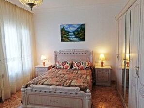 Een slaapkamer met een groot bed, twee nachtkastjes, een kledingkast en een schilderij aan de muur.