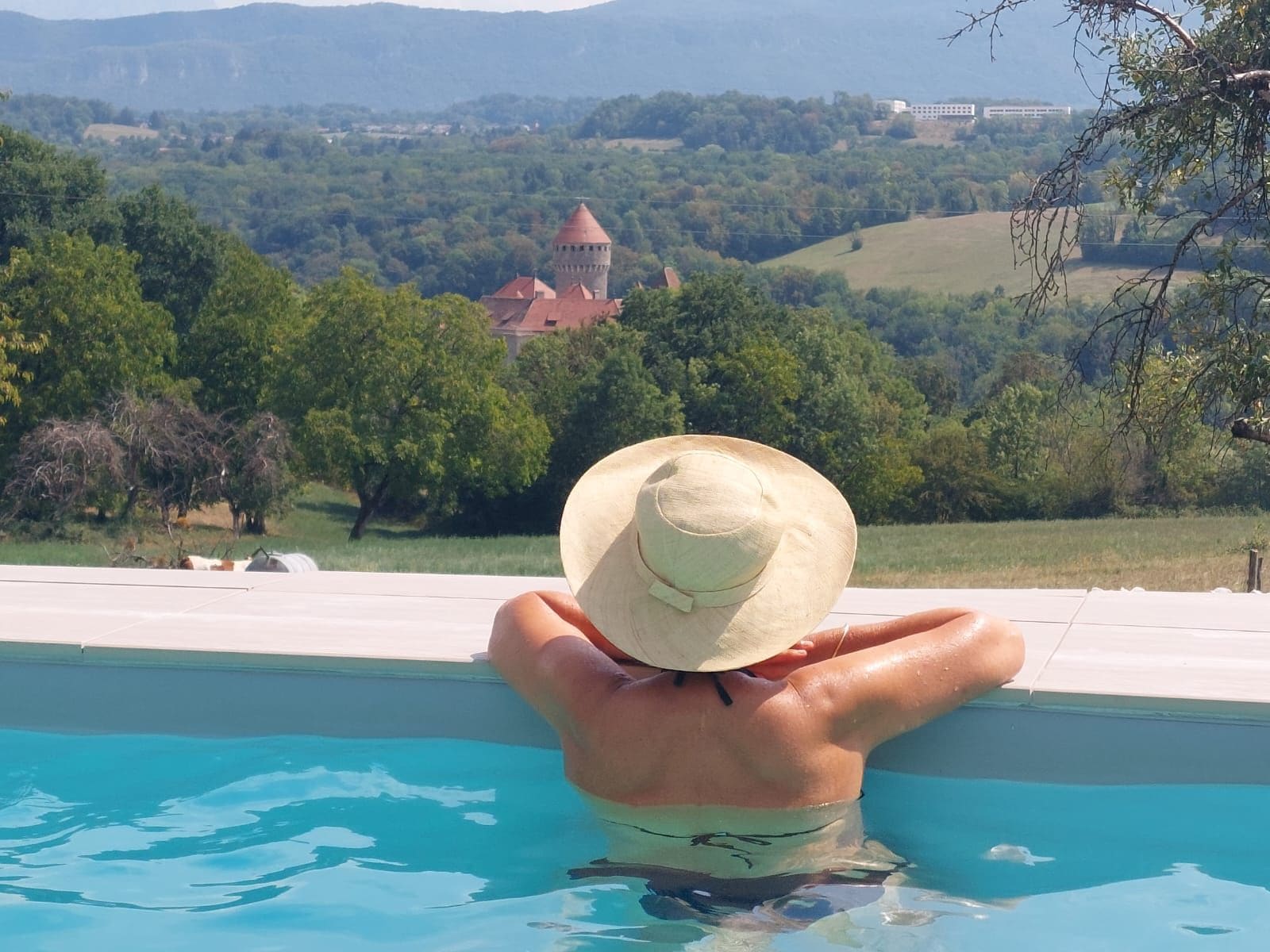 Una persona en una piscina con vistas a una torre y follaje al fondo.