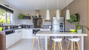 Une cuisine moderne dotée d’un îlot central, de tabourets de bar, d’appareils électroménagers en acier inoxydable et de luminaires suspendus.