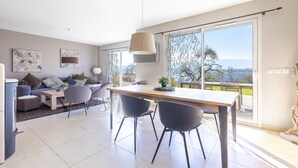 Un salon moderne comprenant un canapé, des fauteuils, une table à manger et une grande fenêtre donnant sur un beau paysage.