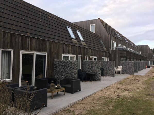 Una fila de cabañas de madera con muros de piedra, asientos exteriores y cielo despejado.