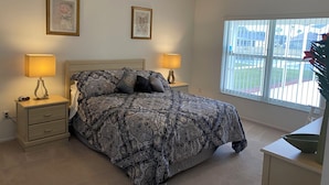 Un dormitorio con cama, dos lámparas de noche, una mesita de noche, una ventana con persianas y un cuadro en la pared.