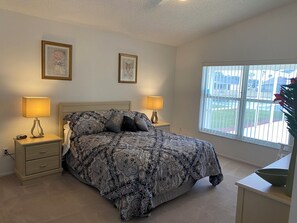 A bedroom with a bed, two bedside lamps, a nightstand, a window with blinds, and a framed picture on the wall.