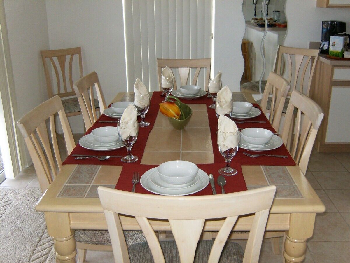 A dining table set for six with white plates, glasses, and a centerpiece.