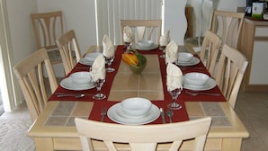 Mesa de comedor preparada para seis personas, con platos blancos, vasos y un centro de mesa.