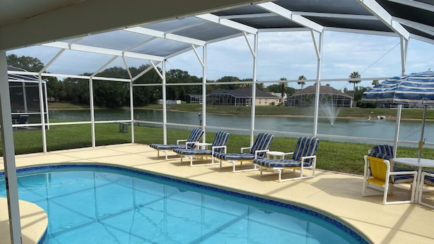 Un área de piscina con zona de estar cubierta y vista al lago.
