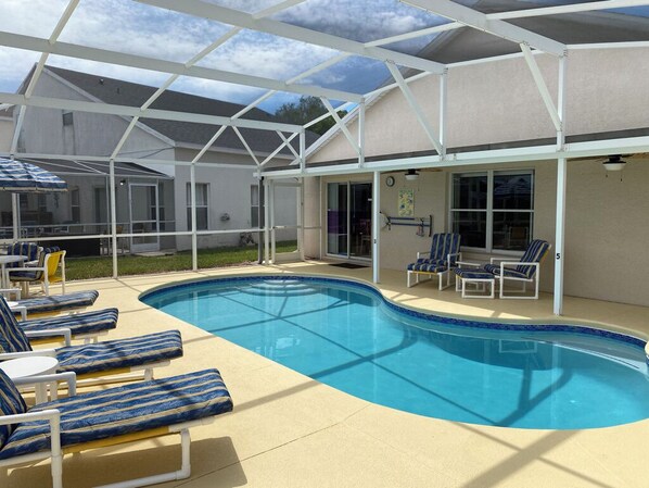 A swimming pool with lounge chairs, a covered patio, and a building with large windows.