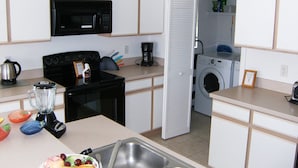 Una cocina compacta con microondas, estufa y lavadora al fondo.