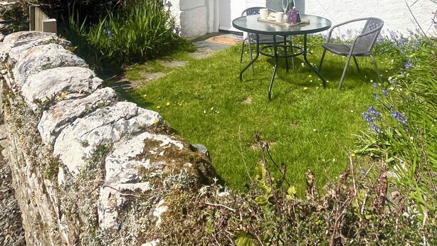 A stone house with a white exterior, a small garden, and a table with chairs outside. - Beautiful Country Cottage (Looe)