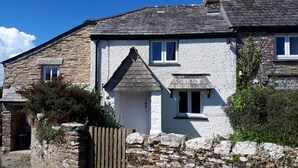 A stone house with a white exterior, a wooden door, and a small window. - Beautiful Country Cottage (Looe)