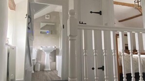 A staircase with white balusters leading to a bedroom with a bed and a nightstand. - Beautiful Country Cottage (Looe)