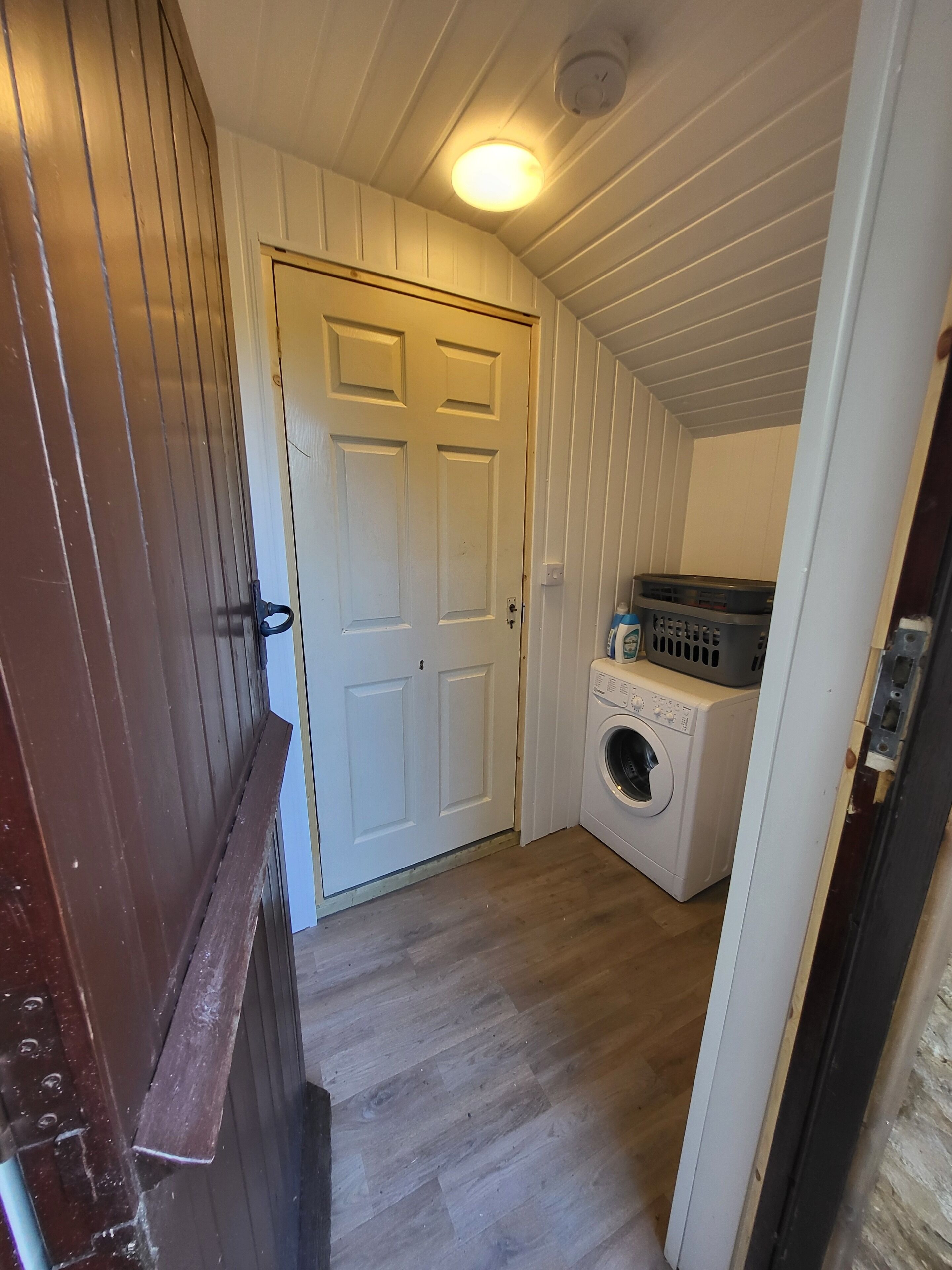 A laundry room with a washing machine and dryer, wooden walls, and a white door.