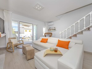 Un salon moderne avec un canapé blanc, des coussins orange, un fauteuil en osier et une table basse en bois.