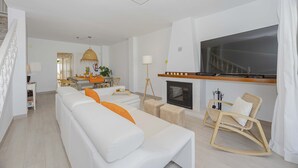 Een moderne woonkamer met een witte bank, een houten schommelstoel, een open haard en een grote televisie.