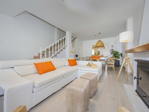 Un salon moderne avec un canapé blanc, des coussins orange, une table basse en bois et une cheminée.