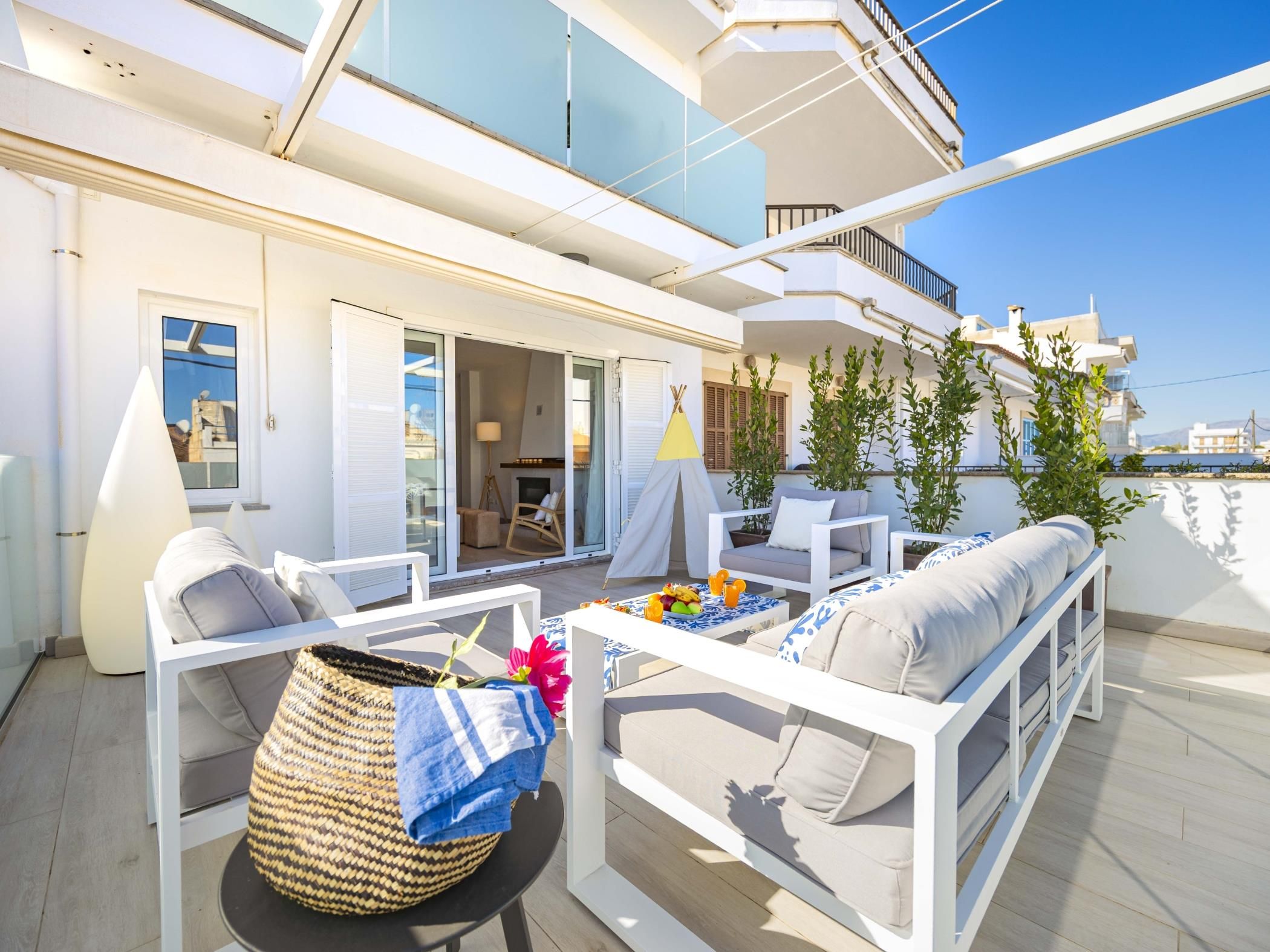An outdoor seating area with white furniture, a woven basket, and a table with fruit and drinks.