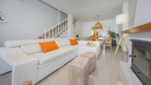 Een moderne woonkamer met een witte hoekbank, een open haard en een eethoek met een tafel en stoelen.