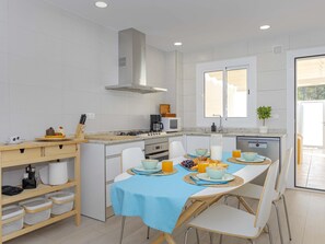 A modern kitchen with white cabinetry, a stainless steel range hood, and a breakfast setup with a blue tablecloth. - Laia House: a semi-detached house for 6 in Can Picafort | 3 bedrooms (Can Picafort)