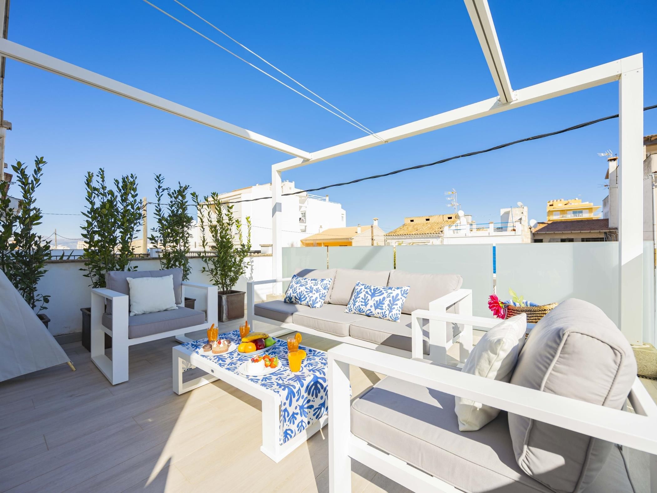 A rooftop terrace with white furniture, a dining table with food, and potted plants.