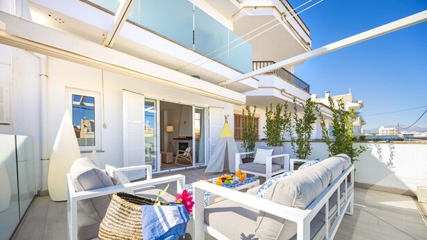 Een modern terras buiten met witte meubels, een eethoek en uitzicht op zee.
